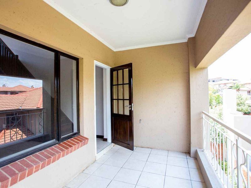A covered balcony featuring tiled flooring, a wrought iron balustrade, and direct access to the interior through a timber-framed glass door.