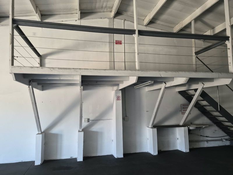 Industrial utility space featuring a mezzanine level with steel balustrades, exposed roof trusses, and a functional sink area, suitable for storage or workshop use.