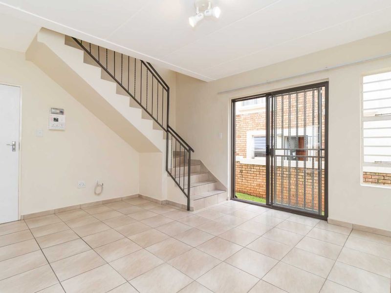 An empty, tiled living area featuring a staircase with a metal balustrade and a sliding glass door leading to the exterior.