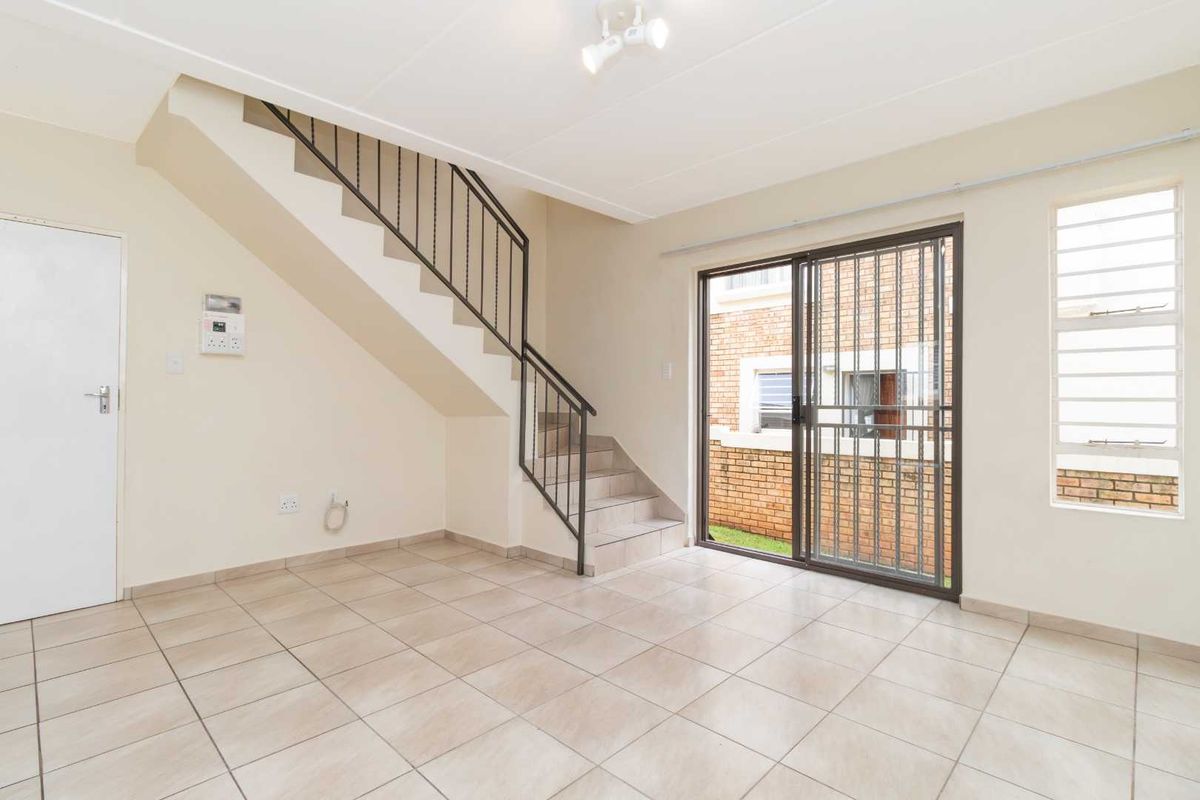 An empty, tiled living area featuring a staircase with a metal balustrade and a sliding glass door leading to the exterior.