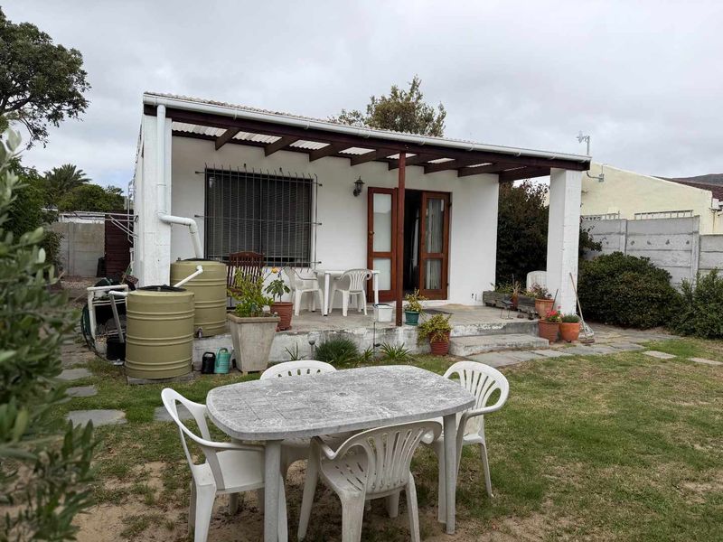 Rear exterior view of the apartment featuring a covered patio area, timber pergola, and rainwater collection tanks set within a private garden space.
