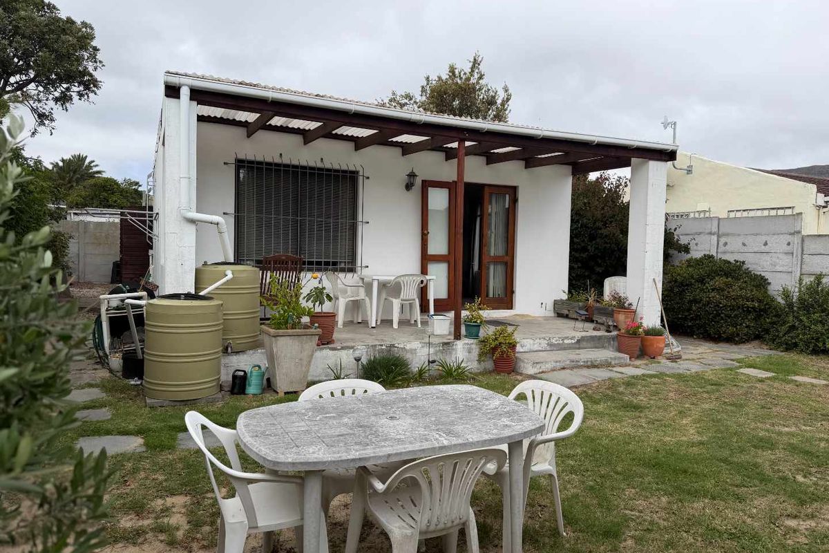 Rear exterior view of the apartment featuring a covered patio area, timber pergola, and rainwater collection tanks set within a private garden space.
