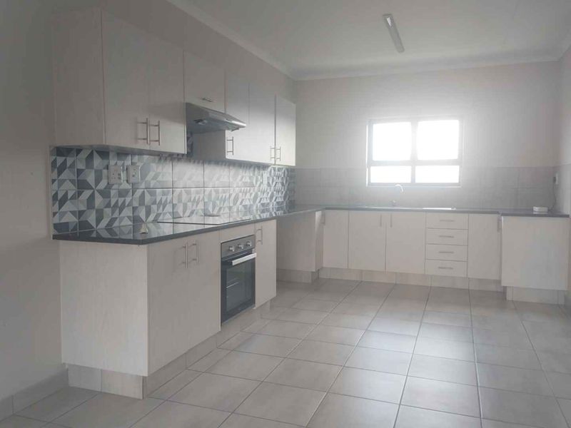 A clean, functional kitchen featuring white built-in cabinetry, a built-in oven with extractor fan, patterned tiled backsplash, and neutral ceramic floor tiles.
