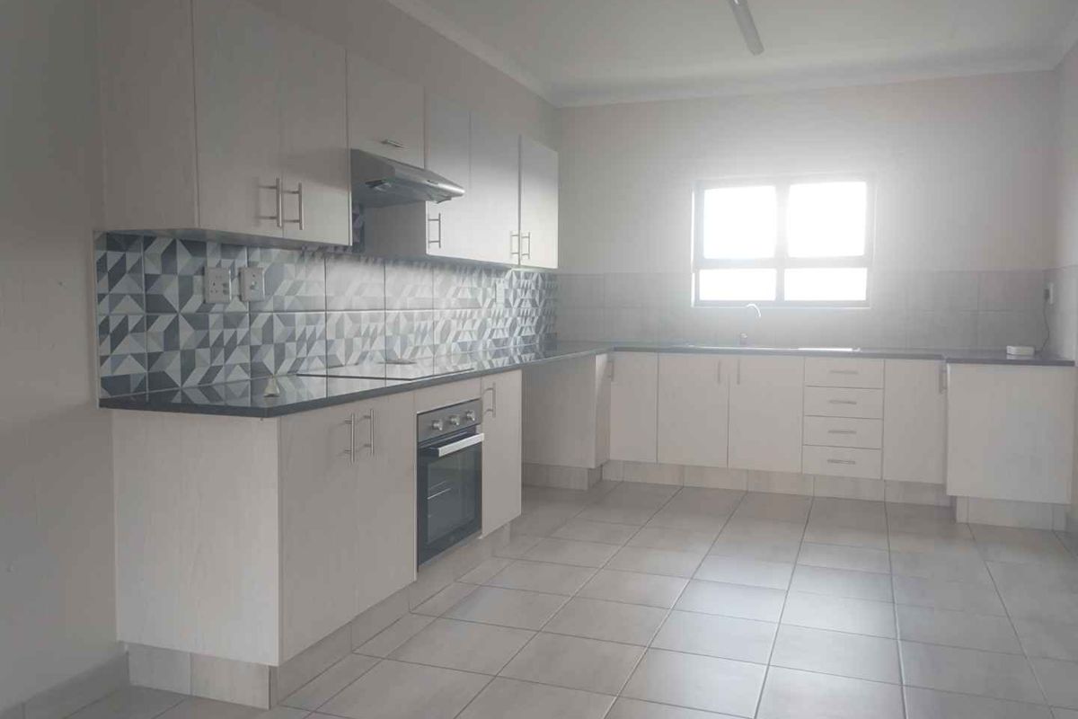 A clean, functional kitchen featuring white built-in cabinetry, a built-in oven with extractor fan, patterned tiled backsplash, and neutral ceramic floor tiles.