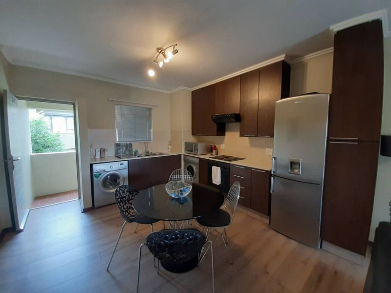 Functional kitchen featuring dark wood cabinetry, laminate flooring, integrated appliances, and direct access to an outdoor balcony area.