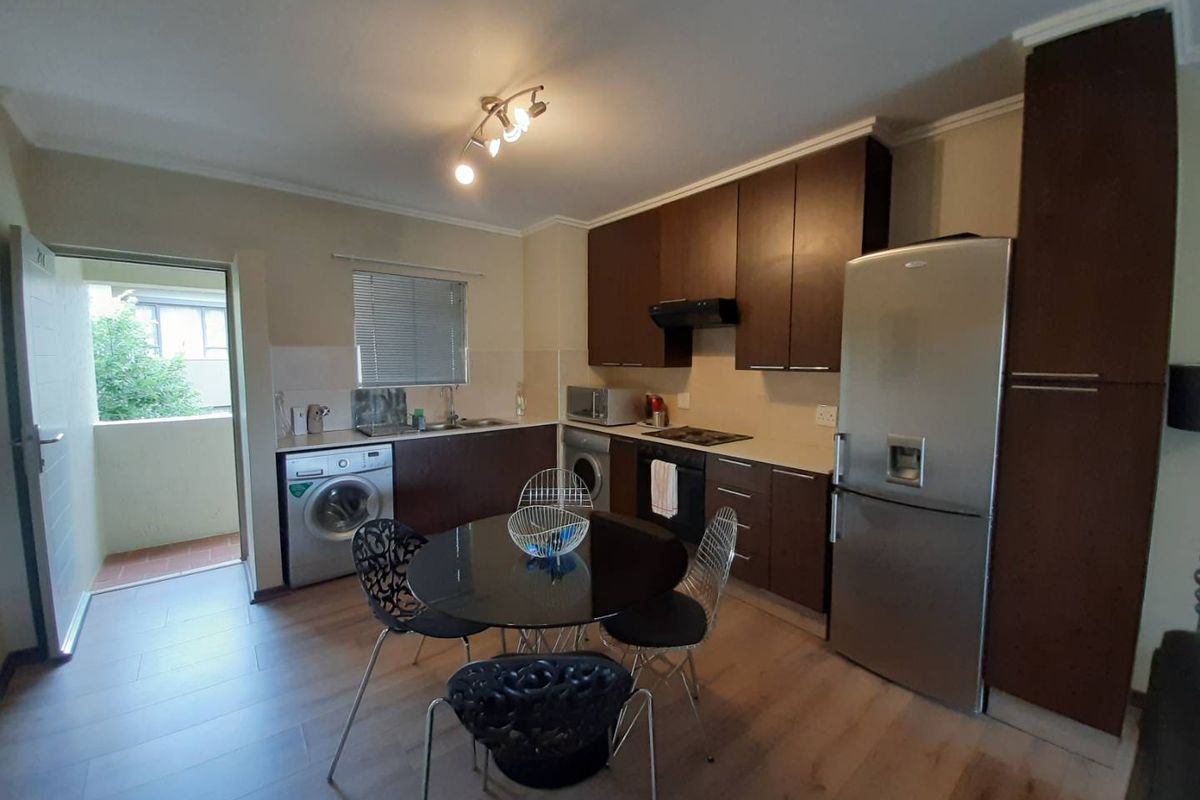 Functional kitchen featuring dark wood cabinetry, laminate flooring, integrated appliances, and direct access to an outdoor balcony area.