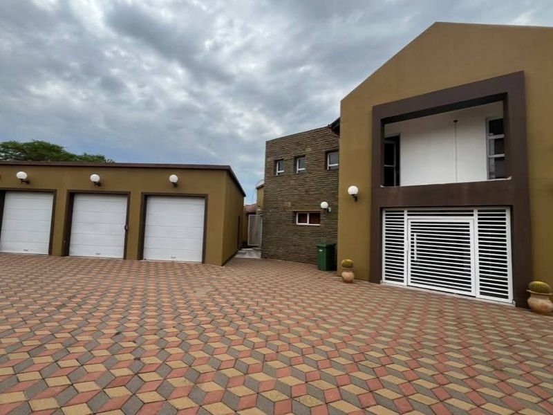 Front exterior view of the property featuring a triple garage, paved driveway, and a secure entrance with modern stone cladding accents.