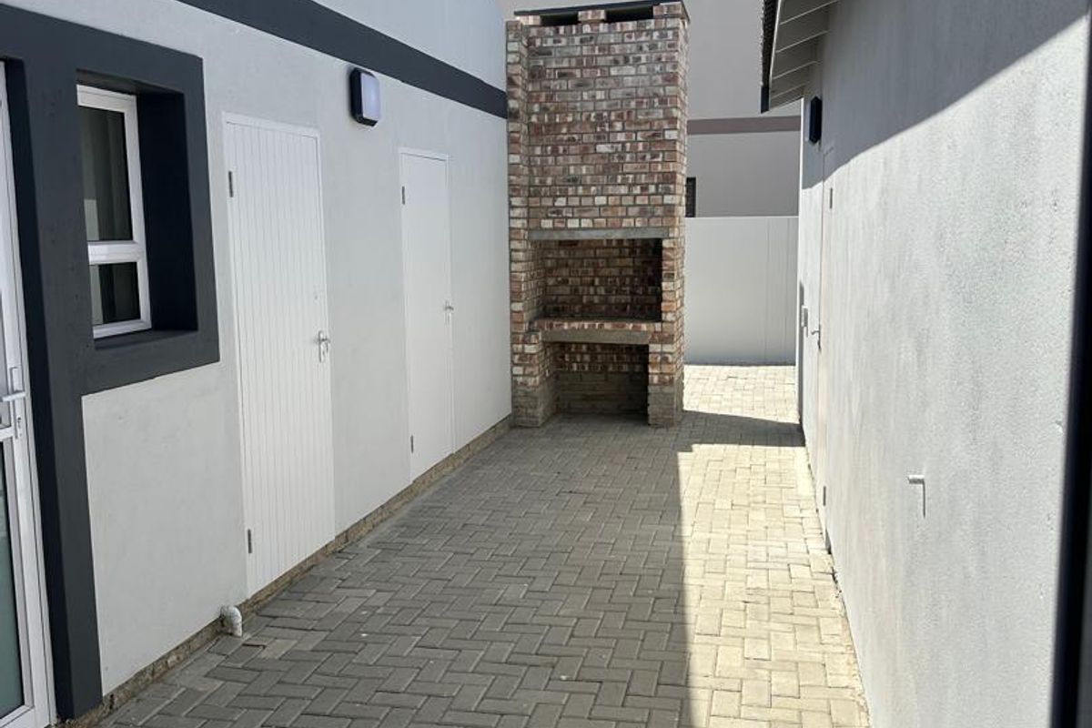 A paved outdoor side courtyard featuring a built-in brick braai or barbecue area, accessible via multiple exterior doors.