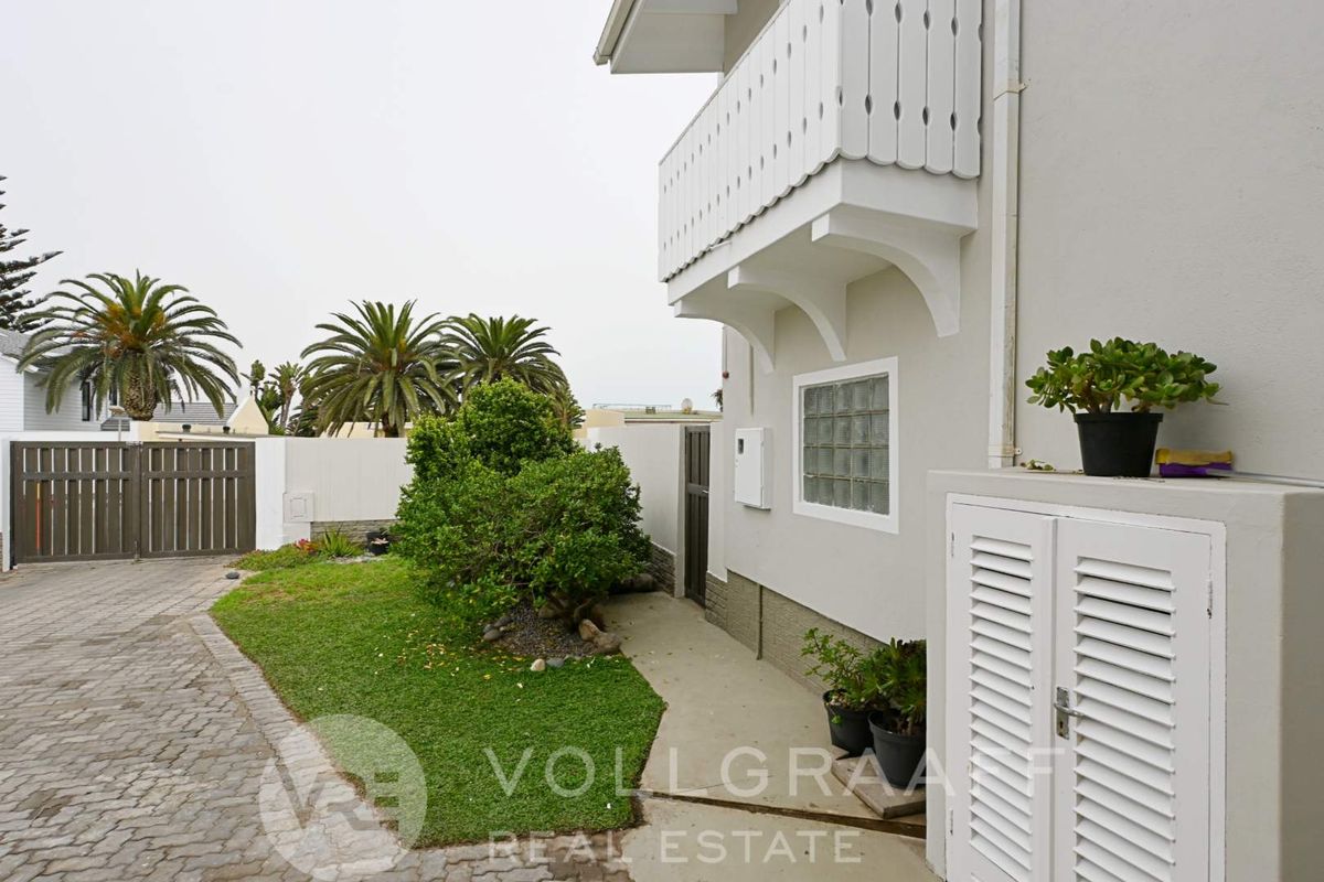 Exterior view of the property featuring a paved driveway, small garden area, and a balcony with white decorative railing.
