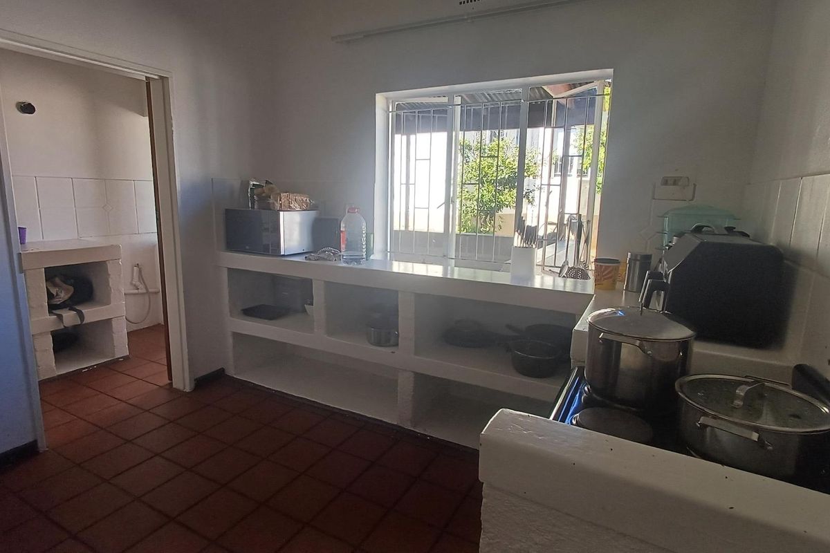 A functional kitchen featuring masonry counters, tiled flooring, and a window with security bars, offering a basic layout ready for modernization.