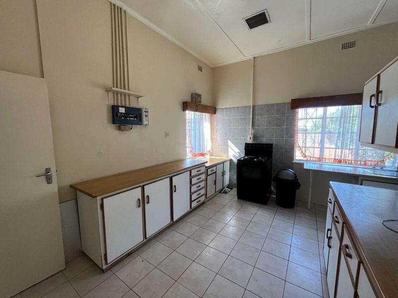 A functional kitchen featuring tiled flooring, built-in cabinetry with laminate countertops, and a freestanding stove, offering potential for modernization.