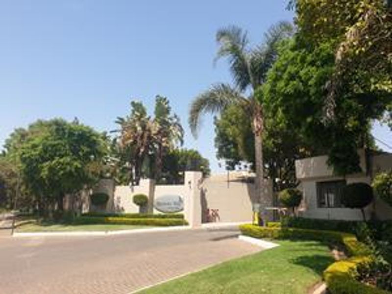 The entrance to the apartment complex features a secure gatehouse, paved driveway, and well-maintained landscaped gardens.