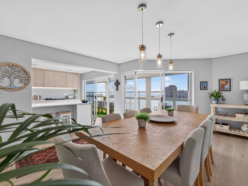 Bright open-plan living and dining area featuring a modern kitchen with island, pendant lighting, and sliding doors leading to a balcony with views.