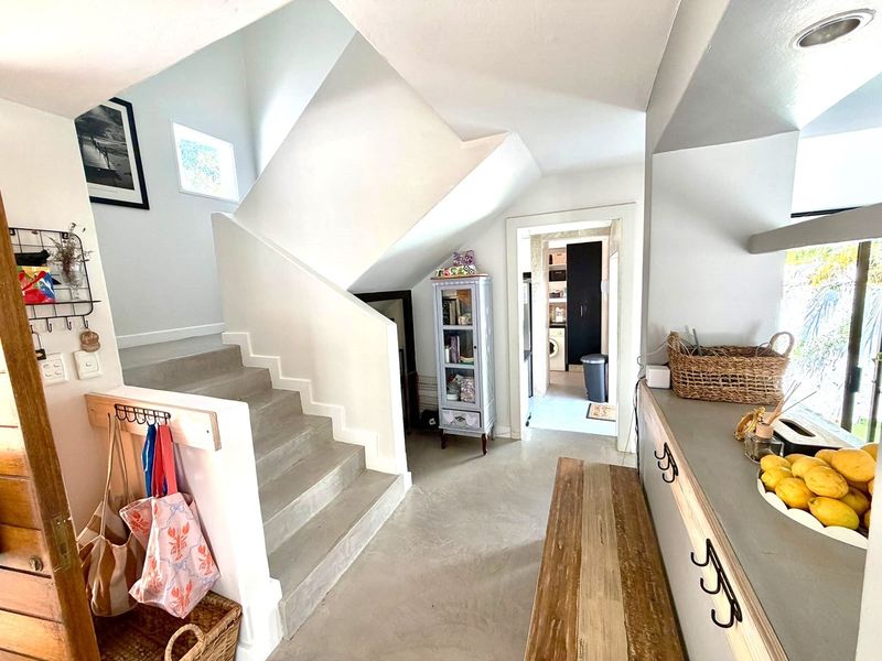 An inviting entryway featuring a modern staircase with concrete steps, polished concrete flooring, and a seamless transition into the adjacent utility and kitchen areas.