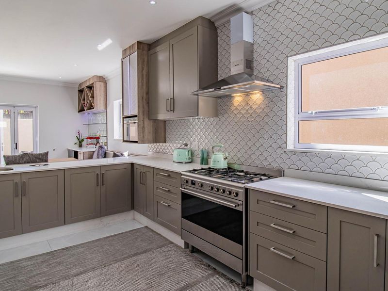 Modern kitchen featuring grey cabinetry, quartz countertops, a gas stove with extractor fan, and a stylish scalloped tile backsplash.