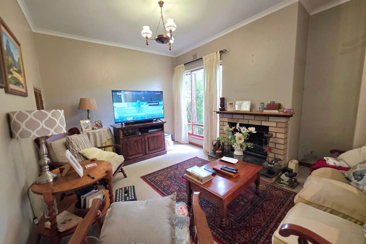 A traditional living room featuring a brick fireplace, cove cornicing, and large windows with security bars, offering a cozy and functional living space.