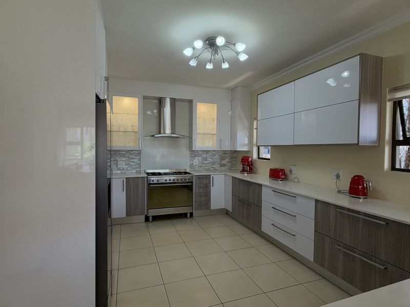 Modern kitchen featuring sleek two-tone cabinetry, stone countertops, a gas stove with extractor fan, and tiled flooring with ample storage space.