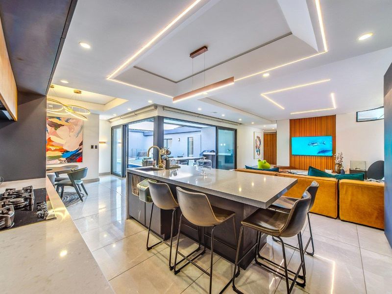 Modern open-plan living area featuring a sleek kitchen island, stone countertops, gas cooktop, and seamless indoor-outdoor flow through large sliding glass doors.