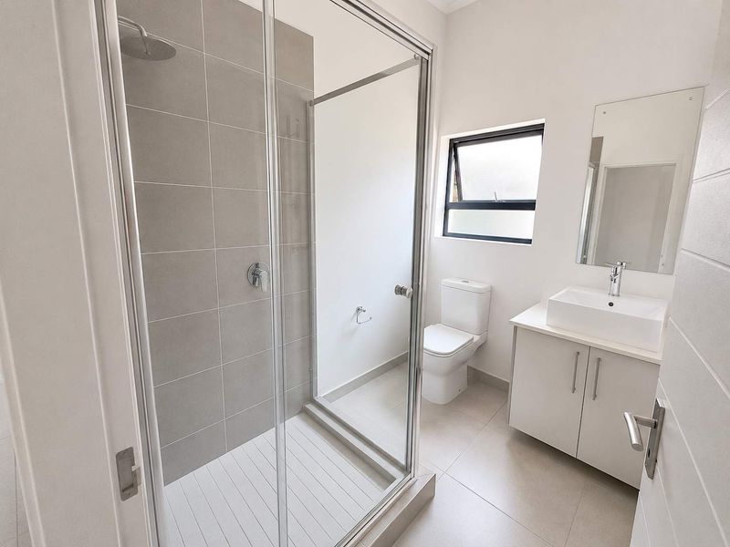 Modern bathroom featuring a glass-enclosed shower with rain head, a sleek vanity with vessel sink, and neutral floor-to-ceiling tiling.