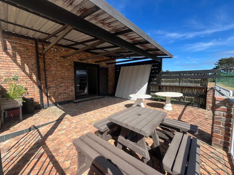 Covered outdoor patio area featuring brick walls, paved flooring, and a metal roof structure, providing a functional space for outdoor relaxation.