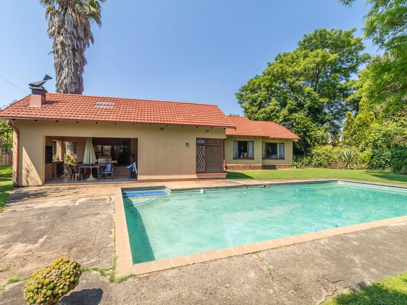 Rear view of the property featuring a swimming pool, covered patio area, and established garden with a tiled roof structure.
