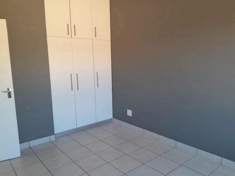 A clean, empty bedroom featuring neutral grey walls, white built-in cupboards, and light-colored tiled flooring.
