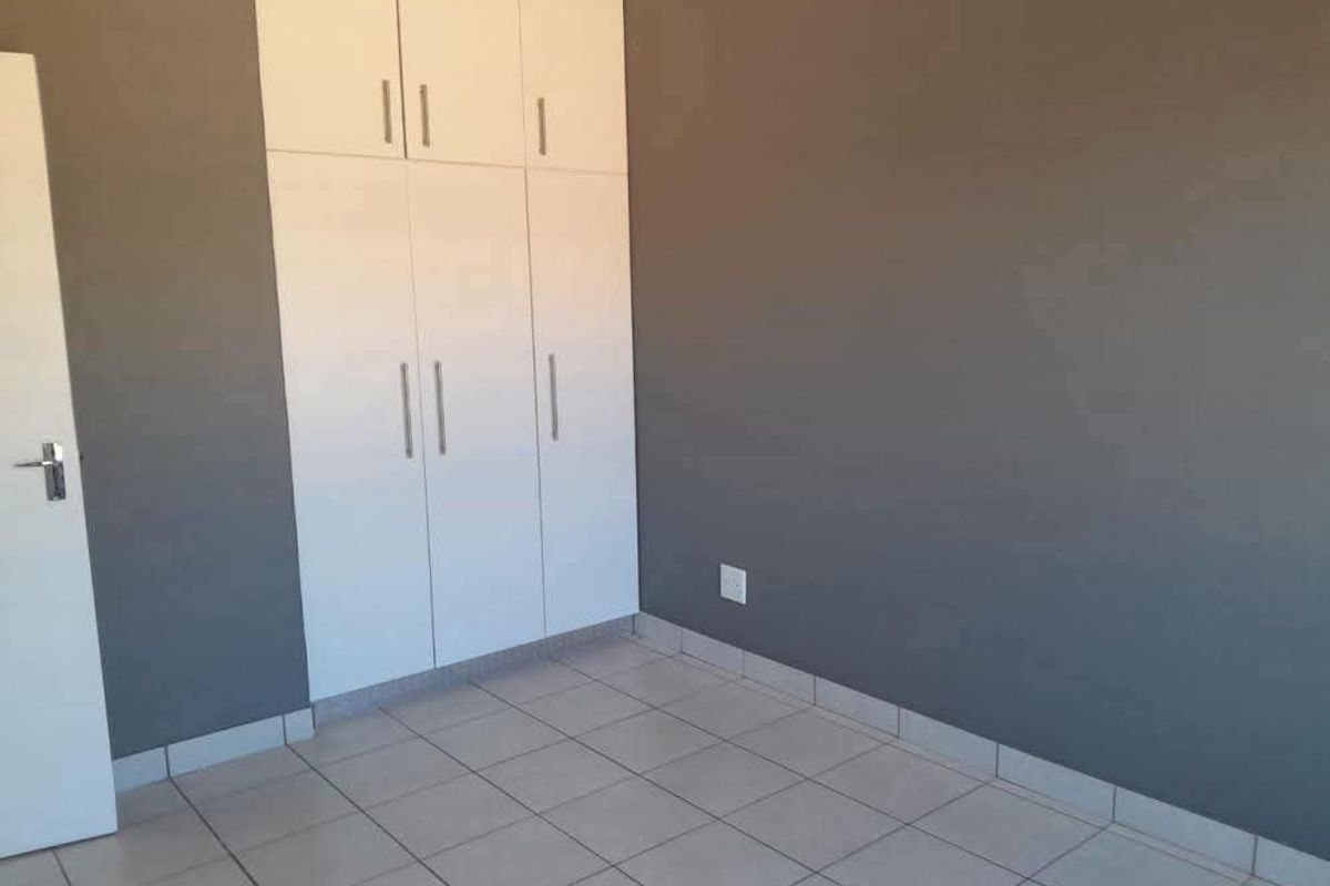 A clean, empty bedroom featuring neutral grey walls, white built-in cupboards, and light-colored tiled flooring.