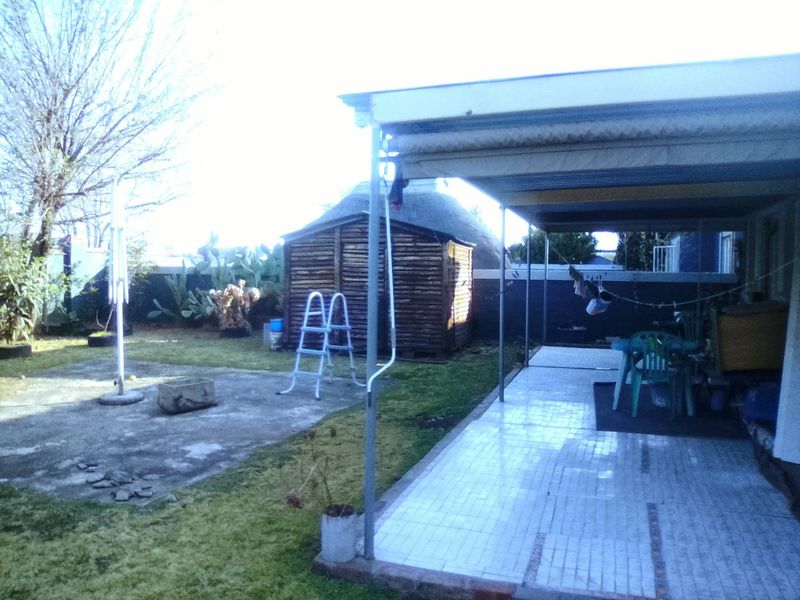A covered patio area overlooking a garden with a detached wooden shed and boundary walling.