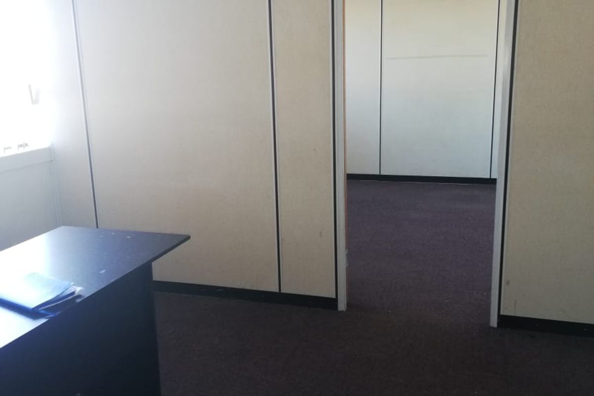 An empty office space featuring modular partition walls, suspended ceiling tiles, and carpet flooring, offering a functional layout for professional use.