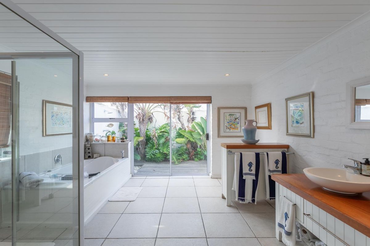 Spacious bathroom featuring a built-in bathtub, glass-enclosed shower, and a wooden vanity with vessel sinks, opening directly onto a private garden patio.