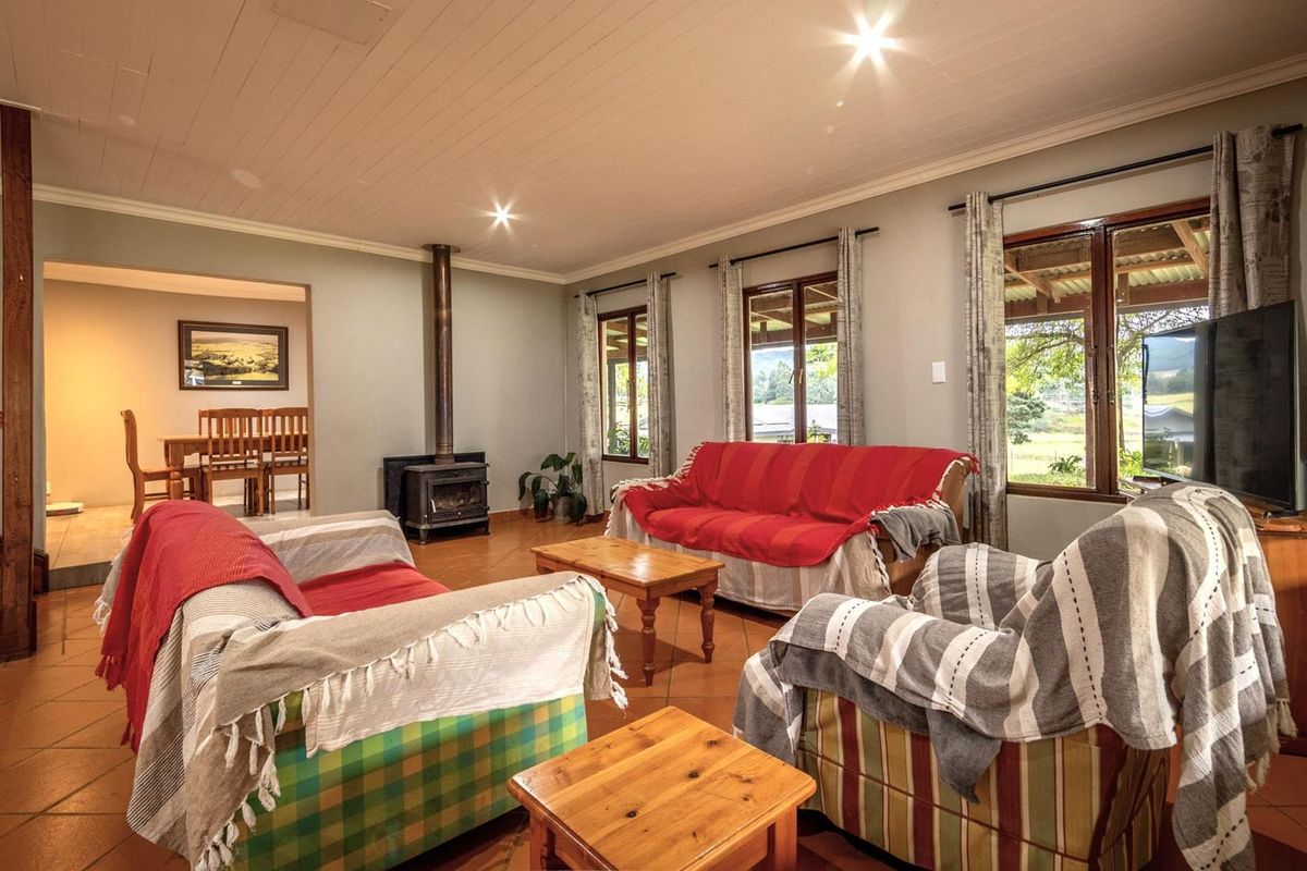Spacious living room featuring terracotta floor tiles, a freestanding wood-burning fireplace, and large timber-framed windows overlooking the garden.