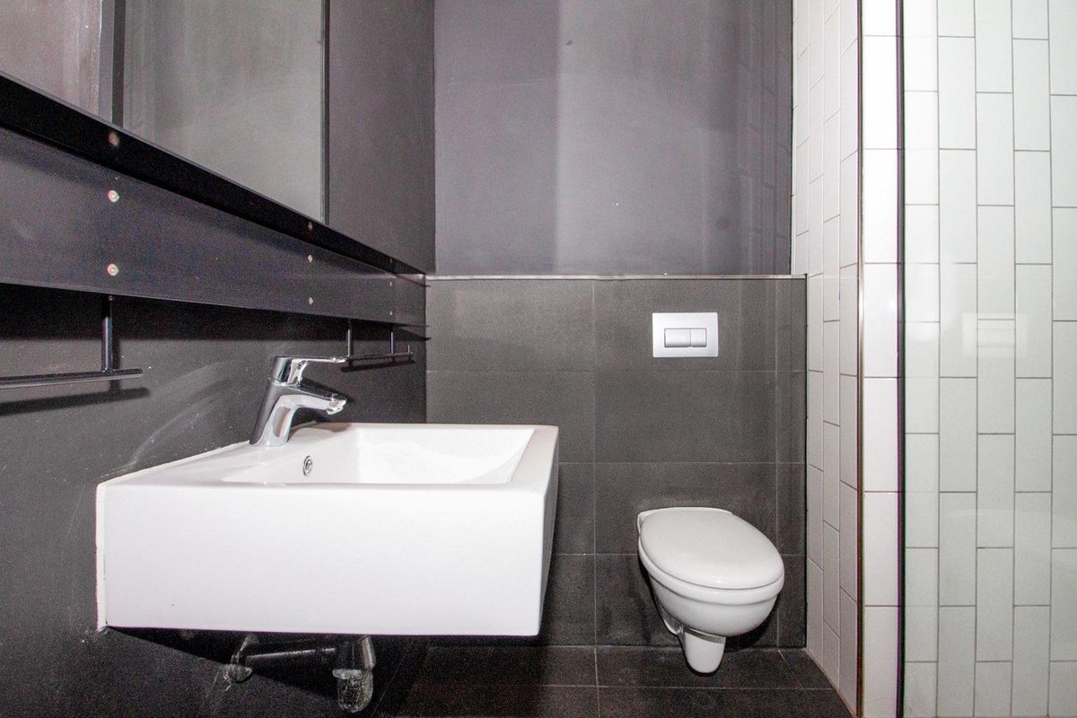 Modern bathroom featuring a wall-mounted basin, a concealed cistern toilet, and dark tiled walls with contrasting white subway tile accents.