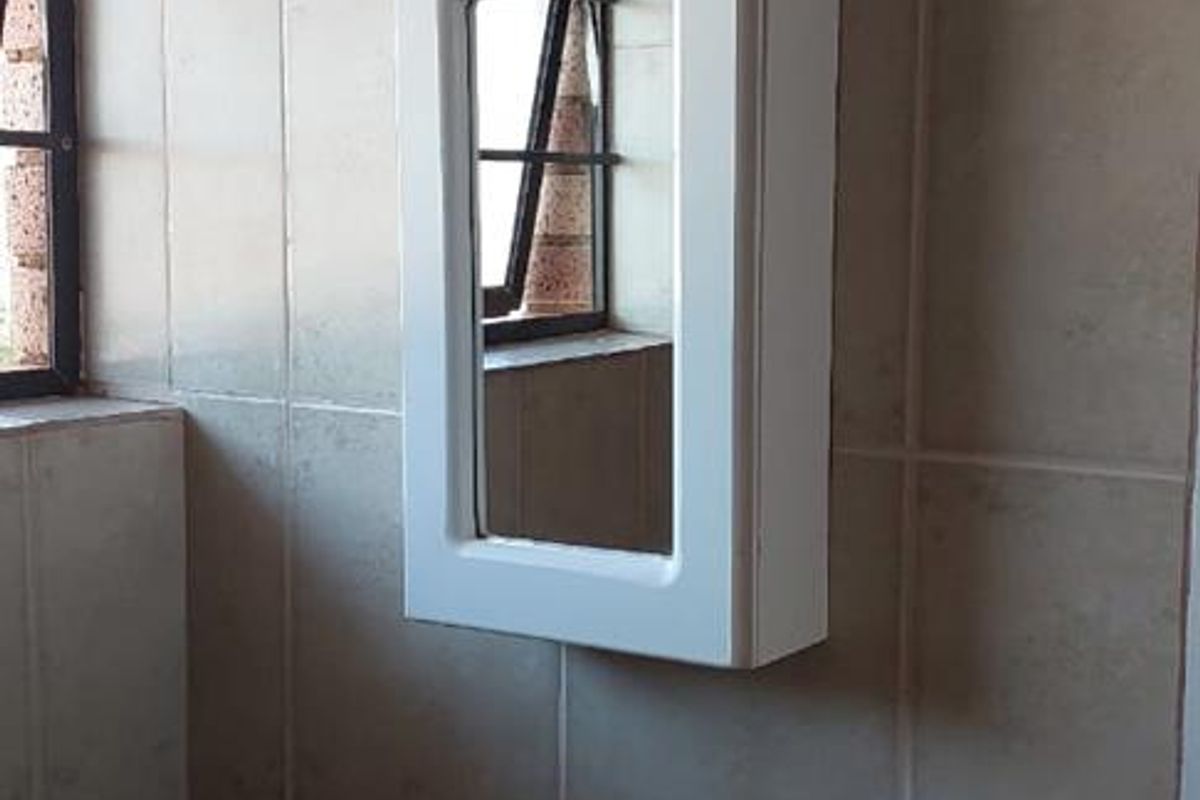 A functional bathroom featuring a wall-mounted vanity mirror cabinet, ceramic basin with chrome taps, and tiled walls.