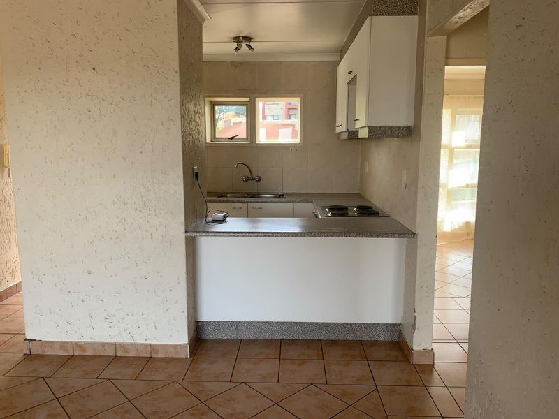 A compact, functional kitchen featuring built-in cabinetry, a breakfast counter, electric hob, and tiled finishes, presenting an opportunity for modern cosmetic updates.