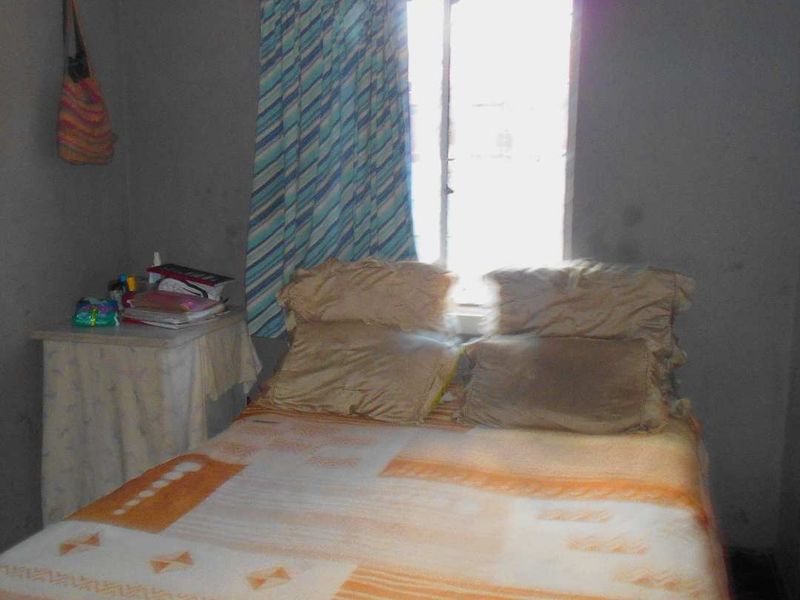 A simple bedroom featuring a window with curtains and plain wall finishes, requiring cosmetic updates to improve the overall aesthetic.