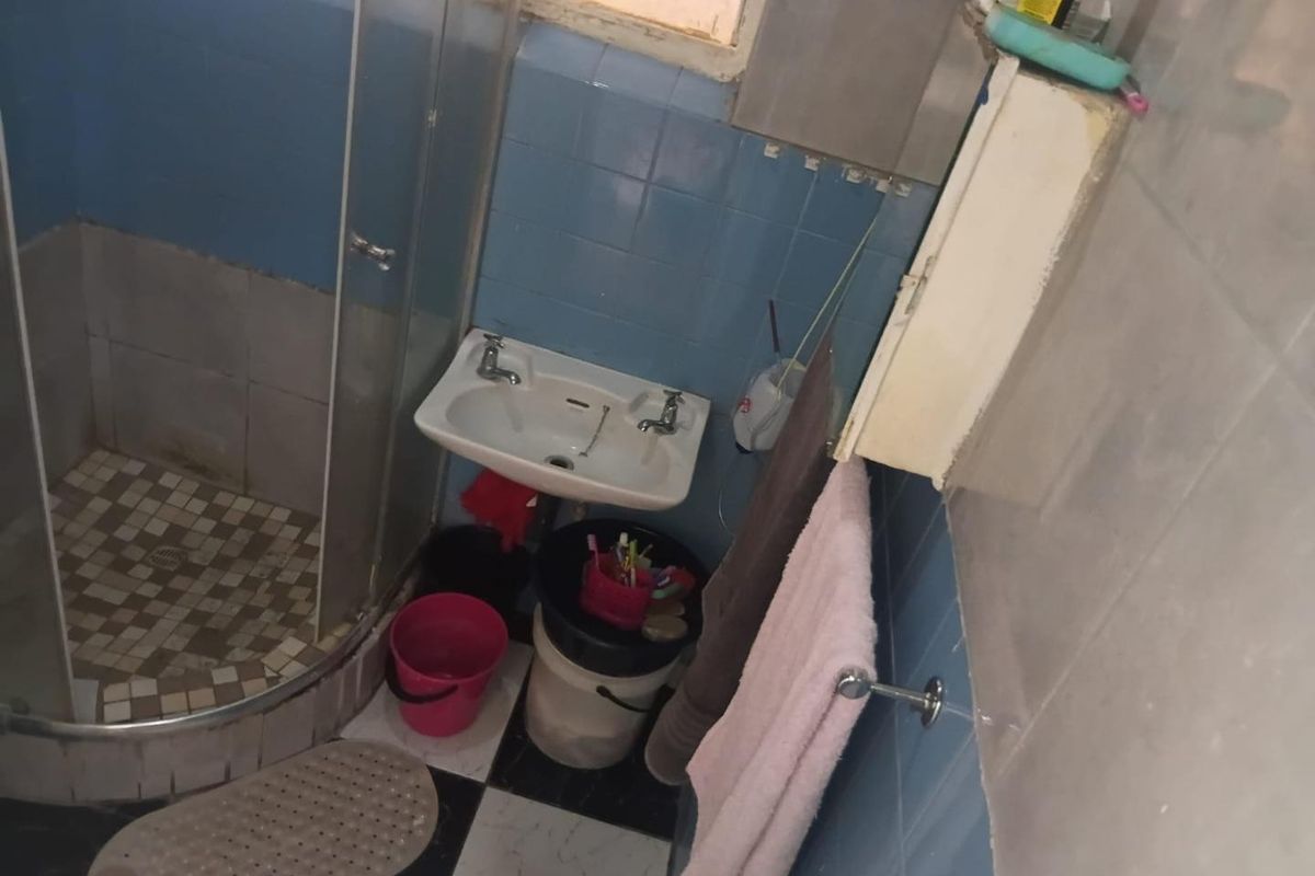 A compact bathroom featuring a shower enclosure, wall-mounted basin, and tiled finishes. The space requires maintenance and cosmetic updates to improve its condition.