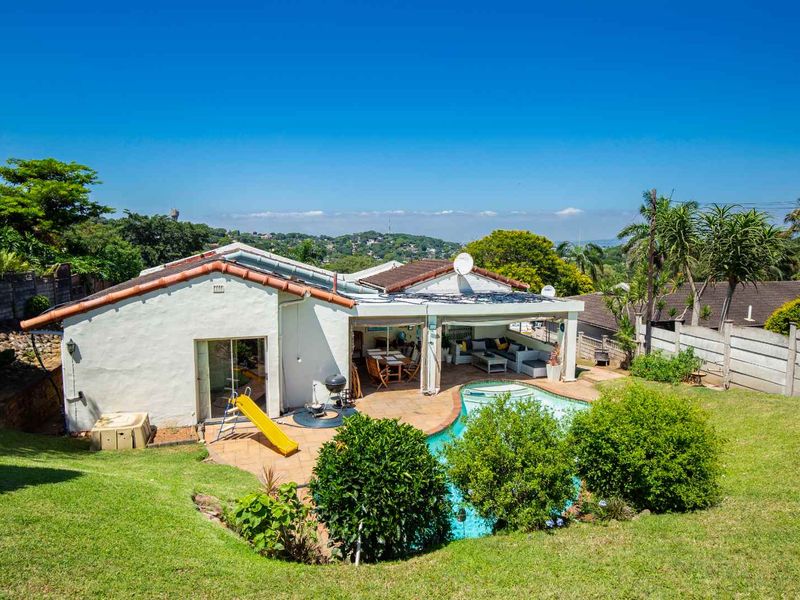 Rear view of the property featuring a swimming pool, paved patio area, and a landscaped garden with distant hillside views.