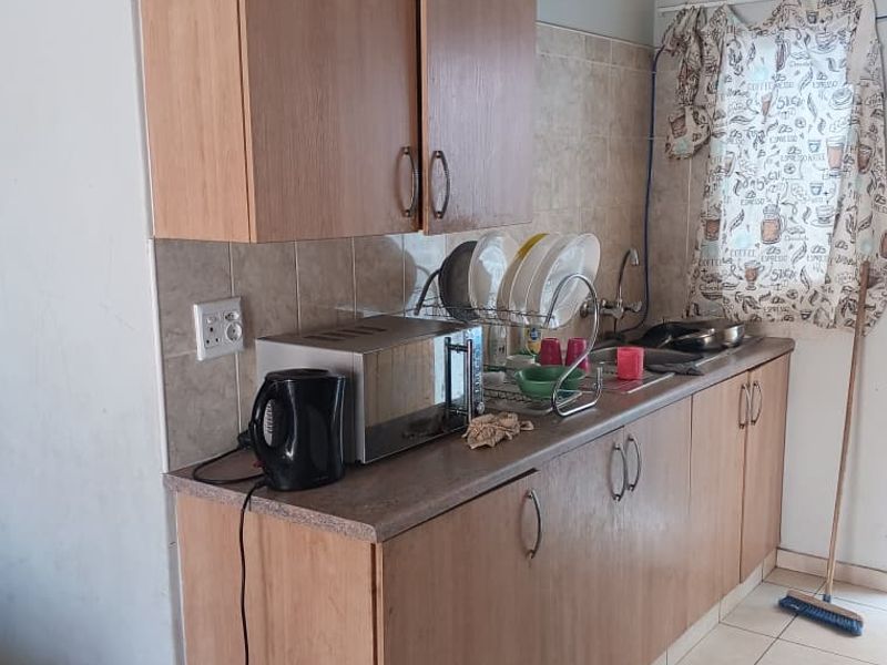 A compact kitchen area featuring laminate cabinetry, tiled backsplash, and ceramic flooring, offering a functional space with potential for modern updates.