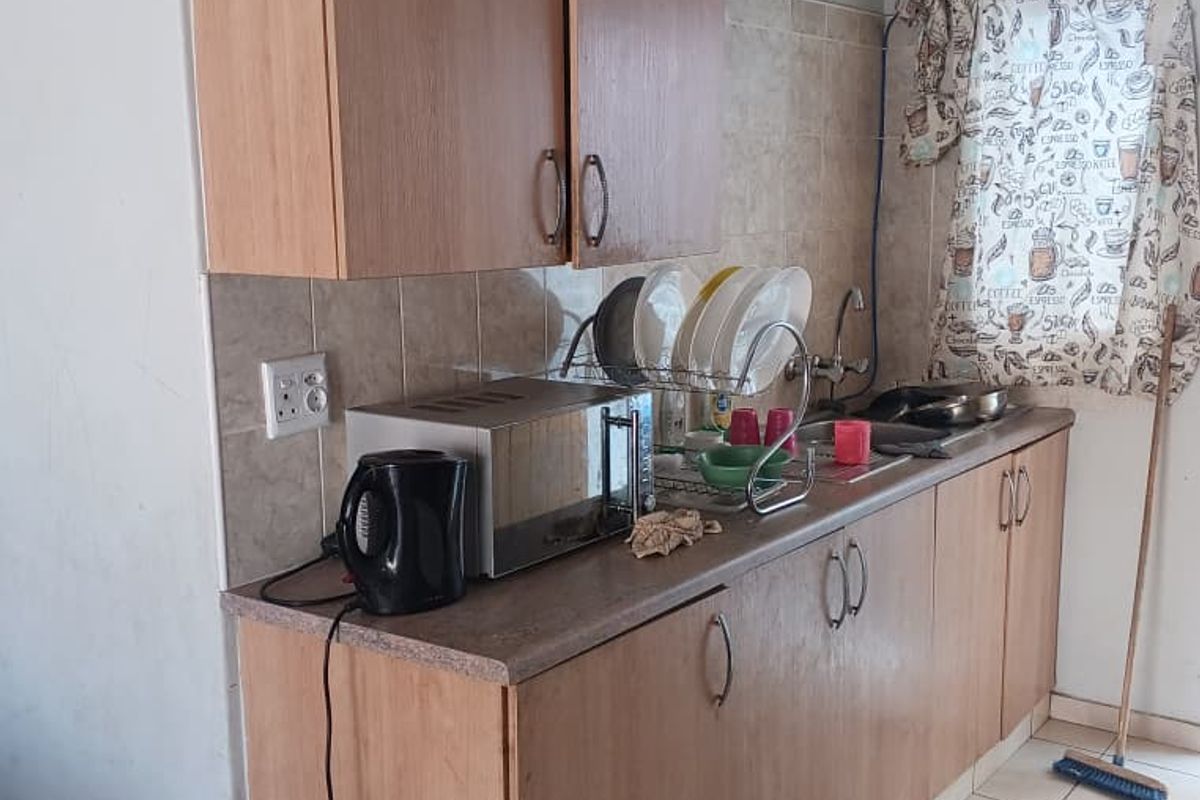 A compact kitchen area featuring laminate cabinetry, tiled backsplash, and ceramic flooring, offering a functional space with potential for modern updates.