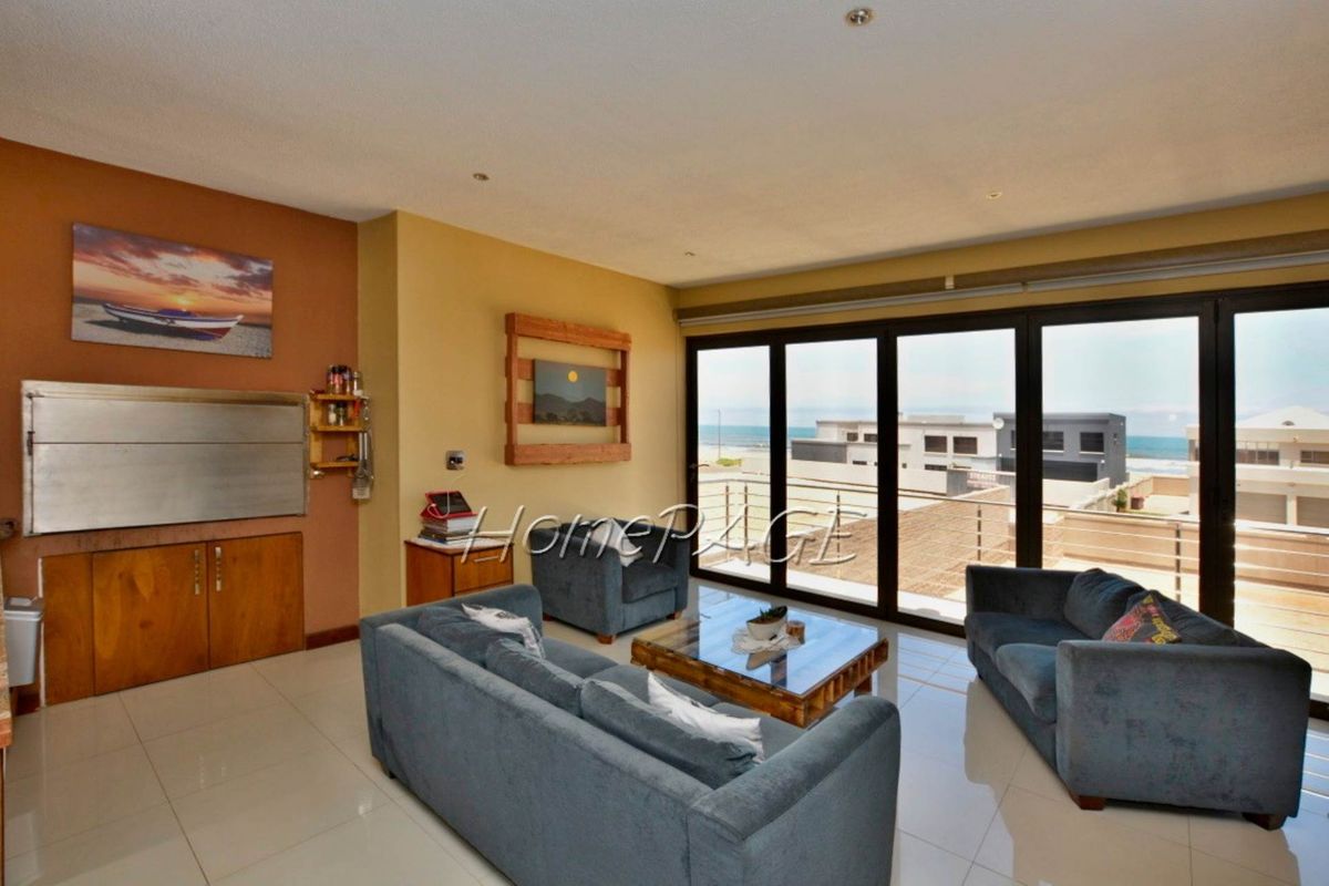 Spacious living area featuring large glass sliding doors opening to a balcony with coastal views and a built-in indoor braai unit.
