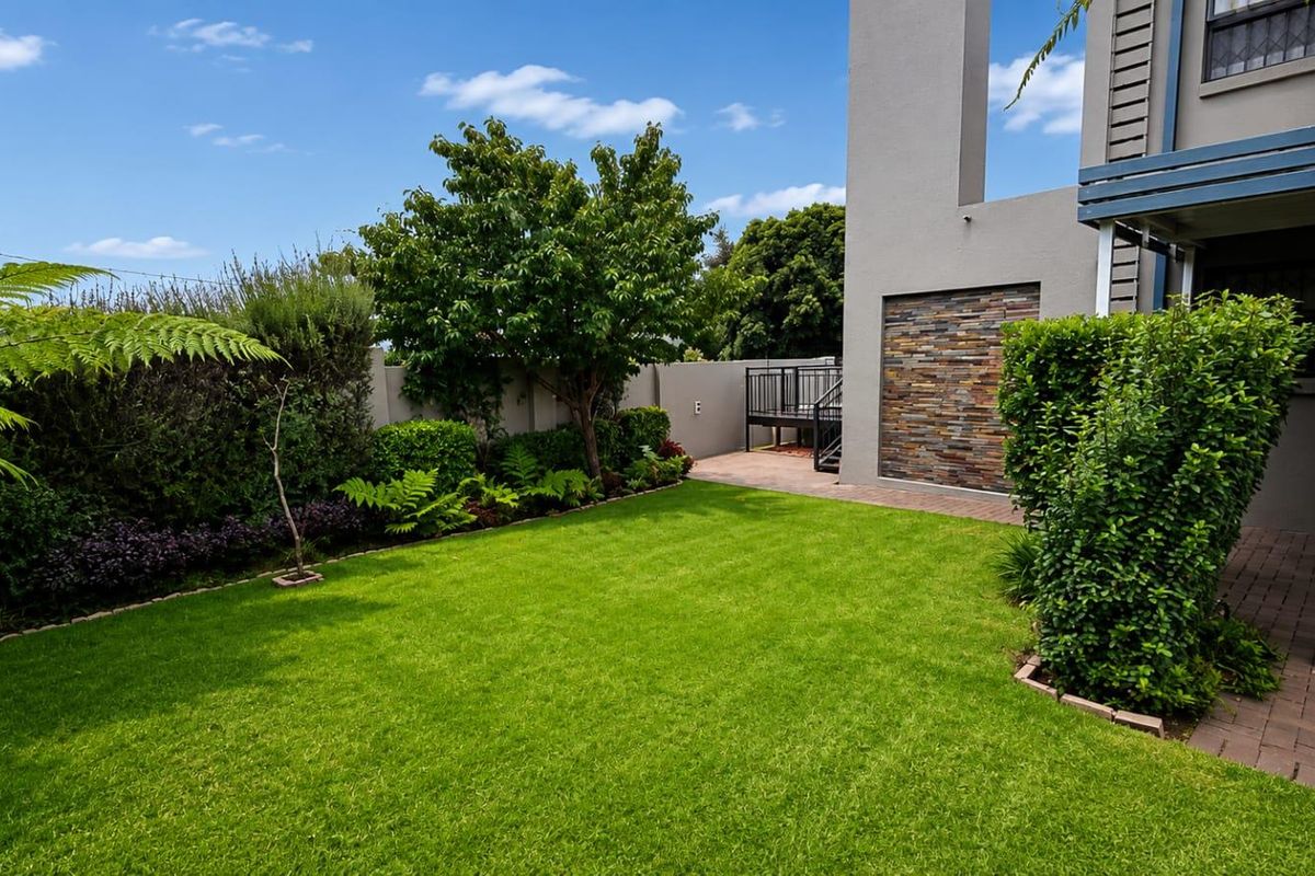 A well-maintained rear garden featuring a manicured lawn, landscaped borders, stone-clad feature wall, and a paved patio area.