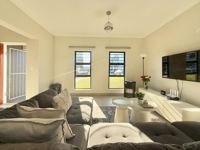 A bright and well-maintained living room featuring tiled flooring, modern aluminium window frames, and neutral wall finishes, offering a comfortable and inviting atmosphere.