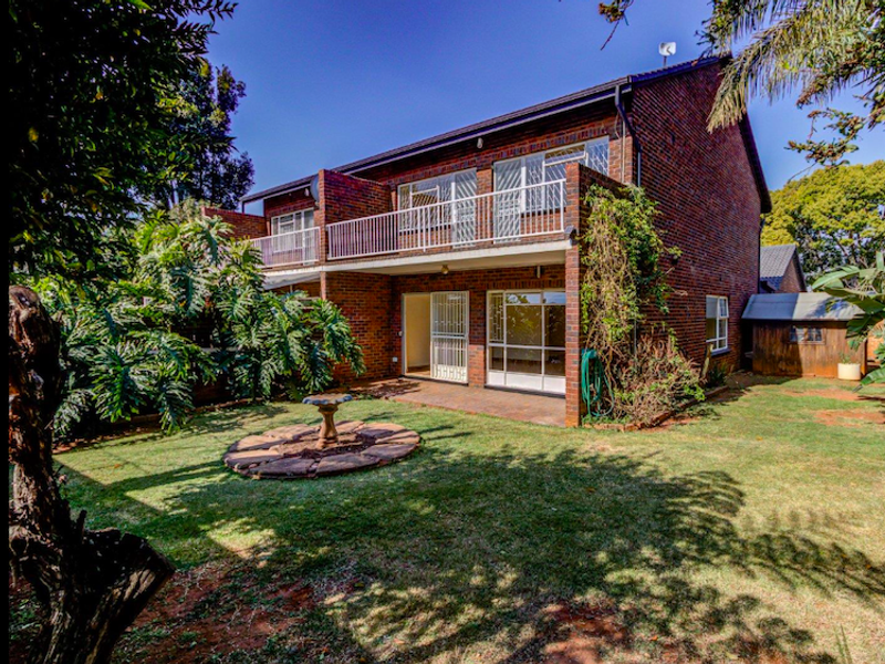 Rear view of a two-story brick townhouse featuring a private garden, paved patio area, and an upper-level balcony with metal railings.