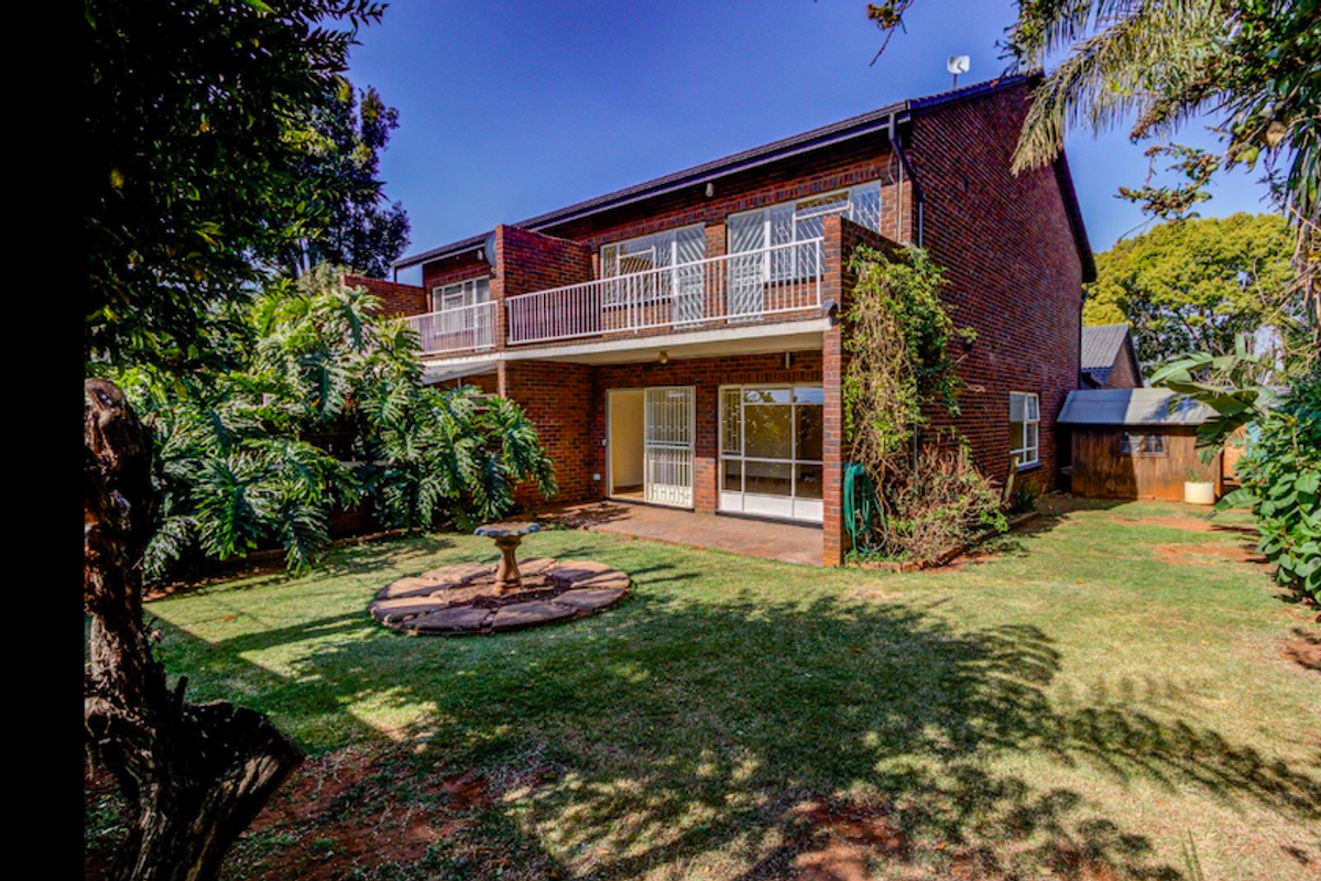 Rear view of a two-story brick townhouse featuring a private garden, paved patio area, and an upper-level balcony with metal railings.