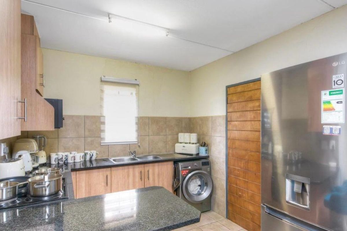 A functional kitchen featuring wood-look cabinetry, granite countertops, a double sink, and space for a washing machine.