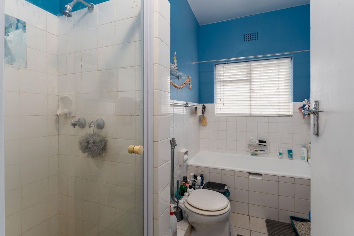 A functional bathroom featuring a separate shower enclosure, a built-in bathtub, and a toilet, finished with white wall tiles and blue painted upper walls.