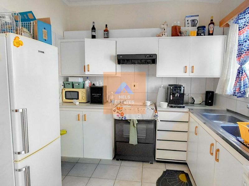 A functional kitchen featuring white cabinetry, tiled flooring, a stainless steel sink, and a built-in extractor fan.