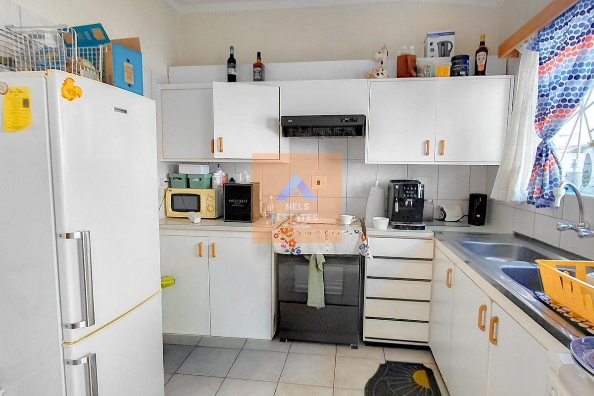 A functional kitchen featuring white cabinetry, tiled flooring, a stainless steel sink, and a built-in extractor fan.