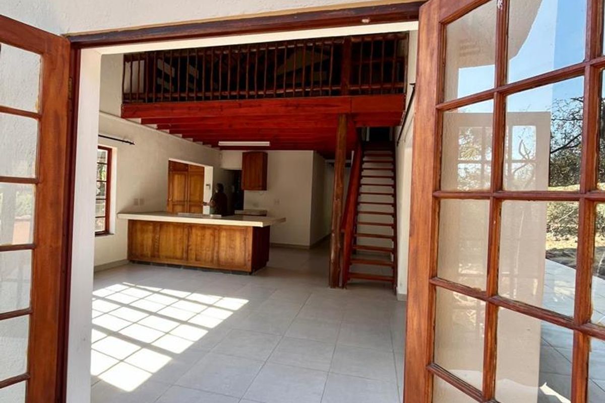 Open plan living area featuring a timber mezzanine level, staircase, and kitchen island, accessible through classic timber french doors.
