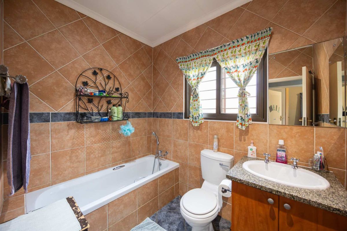 A functional bathroom featuring a bathtub, toilet, and vanity cabinet with a granite countertop and drop-in basin, finished with full-height wall tiling.